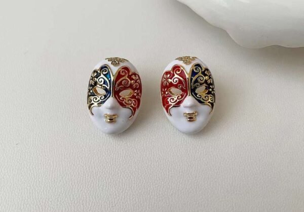 Artistic magical mask face earrings with red and blue enamel detailing and gold accents – statement jewelry from Glowfye